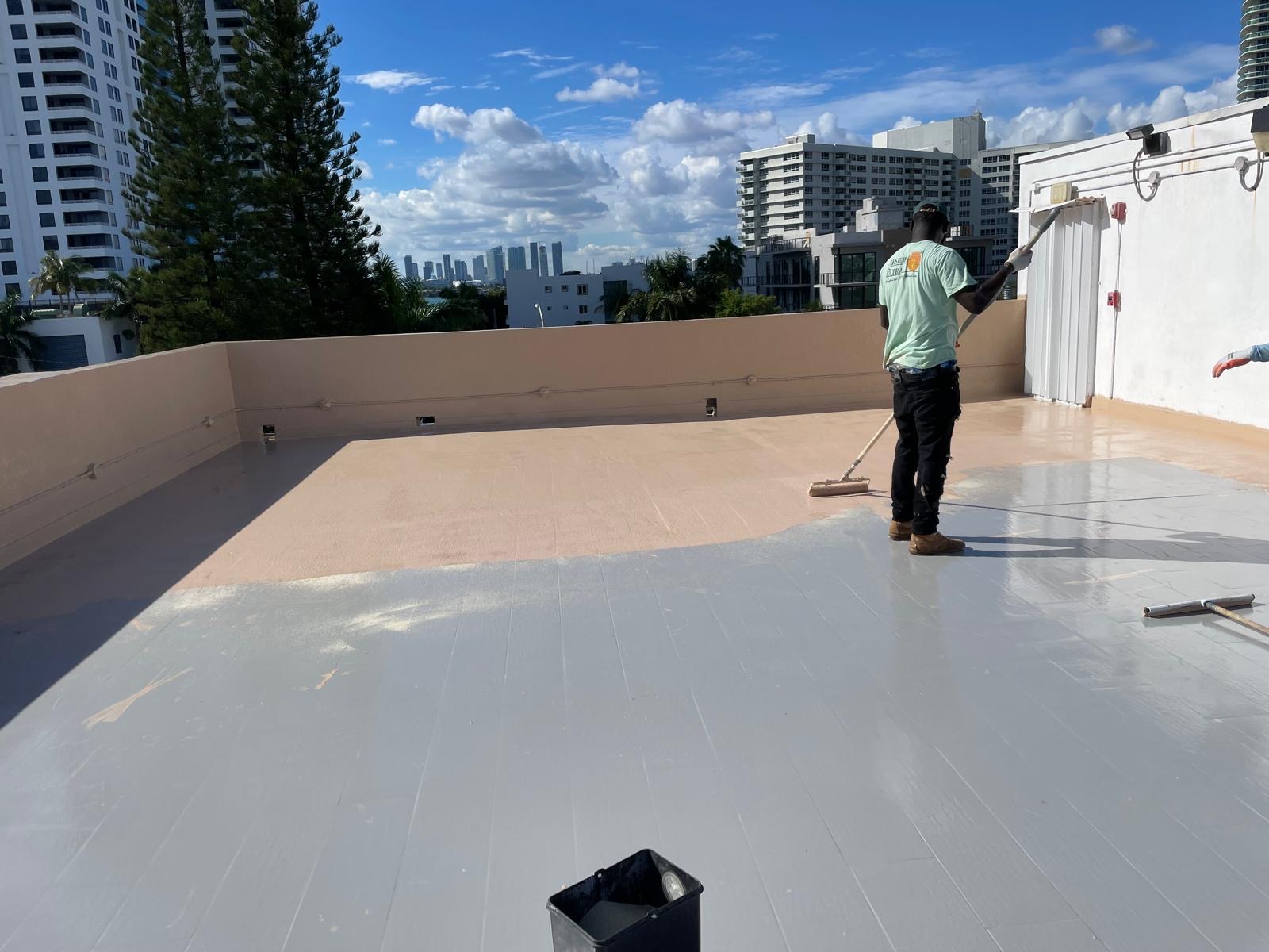 Roofer rolling silicone coating over a Miami Beach flat roof
